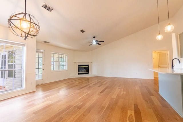 unfurnished living room with light wood finished floors, visible vents, a high end fireplace, a sink, and ceiling fan with notable chandelier