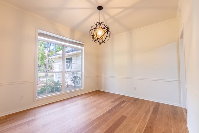 spare room with a chandelier, light wood finished floors, baseboards, and crown molding