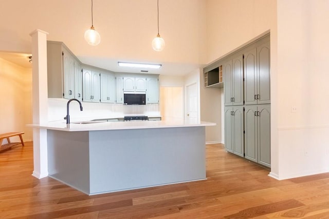 kitchen featuring black microwave, a peninsula, light wood-type flooring, and a sink