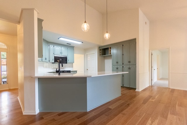 kitchen featuring tasteful backsplash, a peninsula, light countertops, light wood-type flooring, and pendant lighting