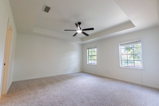 spare room with a raised ceiling, light colored carpet, visible vents, a ceiling fan, and baseboards