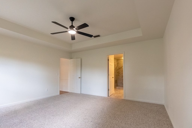 unfurnished bedroom featuring light colored carpet, a raised ceiling, visible vents, and ensuite bath