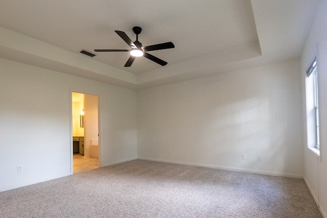 empty room featuring light carpet, ceiling fan, a raised ceiling, and visible vents