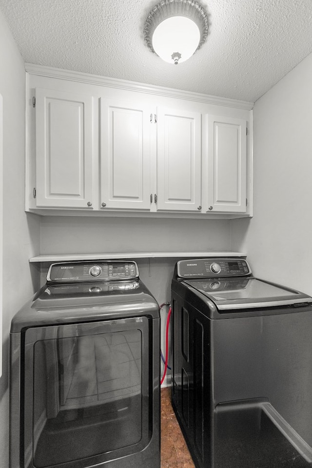 washroom with washer and dryer, cabinet space, and a textured ceiling