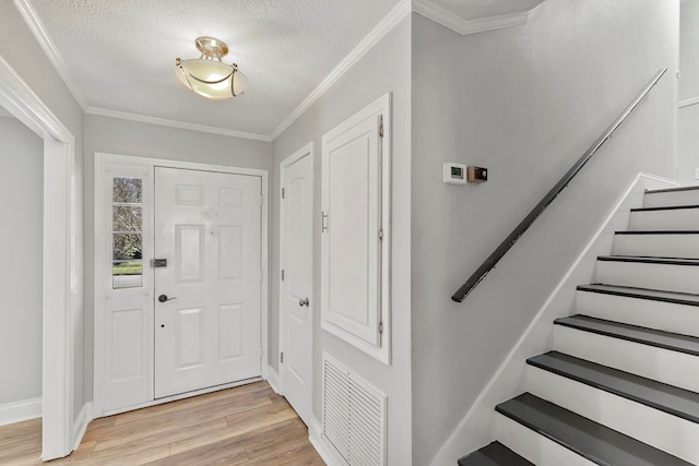 foyer entrance featuring visible vents, light wood-style flooring, a textured ceiling, and crown molding