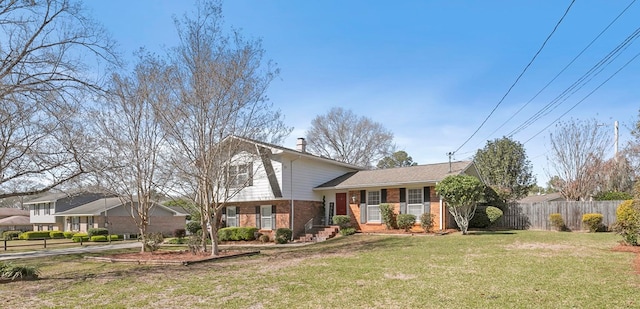 tri-level home with brick siding, a chimney, a front yard, and fence