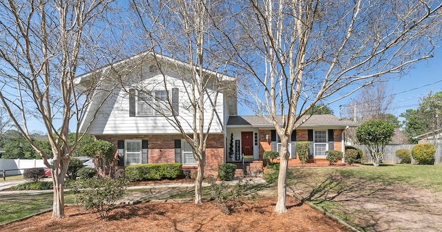 split level home featuring brick siding, a front lawn, and fence