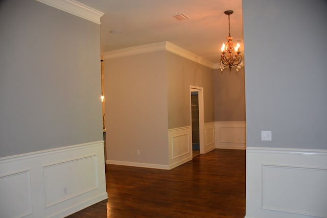 empty room with ornamental molding, wood finished floors, a chandelier, and a wainscoted wall
