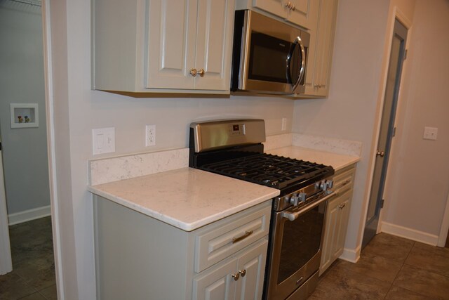 kitchen with white cabinets, baseboards, light countertops, dark tile patterned floors, and appliances with stainless steel finishes