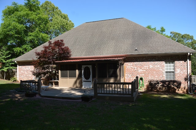 rear view of house with brick siding, roof with shingles, a yard, and a deck