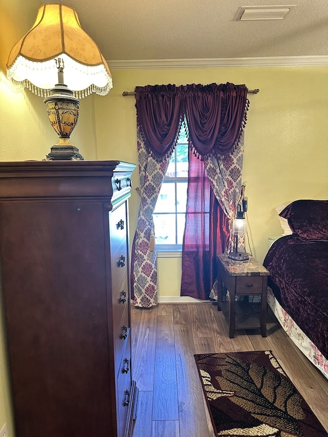 bedroom with a textured ceiling, ornamental molding, wood finished floors, and visible vents