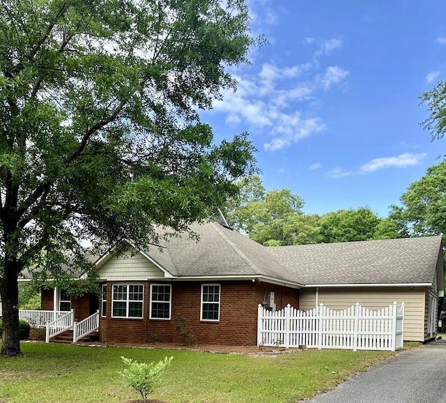 ranch-style house with brick siding, a shingled roof, fence private yard, and a front lawn