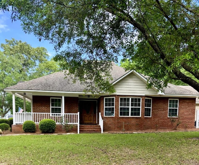 single story home featuring brick siding, roof with shingles, a front yard, and a porch
