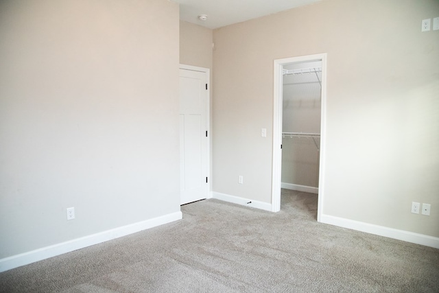 unfurnished bedroom featuring a spacious closet, light colored carpet, and a closet