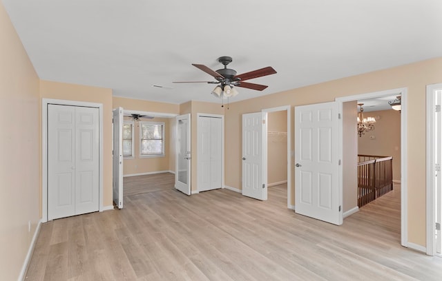 unfurnished bedroom featuring ceiling fan with notable chandelier, light wood-type flooring, and connected bathroom