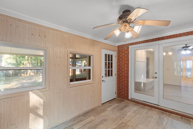 doorway to outside with ceiling fan, wood walls, crown molding, and brick wall