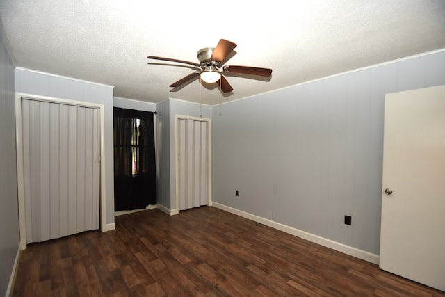 unfurnished bedroom with dark wood-style flooring, a textured ceiling, two closets, crown molding, and ceiling fan
