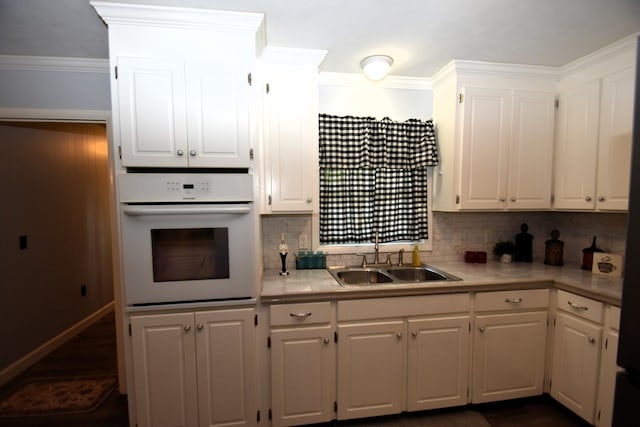 kitchen featuring white oven, light countertops, crown molding, a sink, and white cabinetry