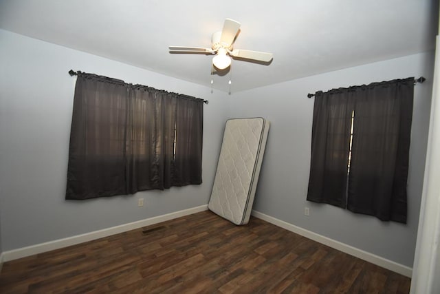 empty room with dark wood-type flooring, baseboards, ceiling fan, and visible vents