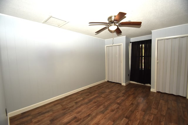 unfurnished bedroom featuring multiple closets, crown molding, baseboards, attic access, and dark wood-style floors