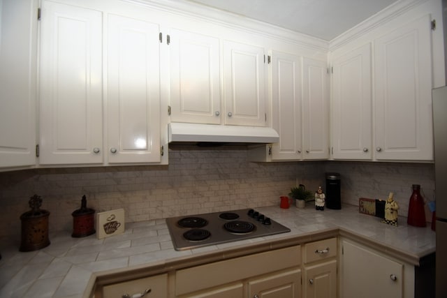 kitchen featuring tile counters, under cabinet range hood, stainless steel electric stovetop, backsplash, and white cabinets
