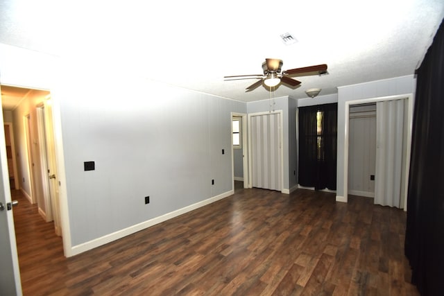 unfurnished bedroom with baseboards, dark wood-style flooring, visible vents, and two closets