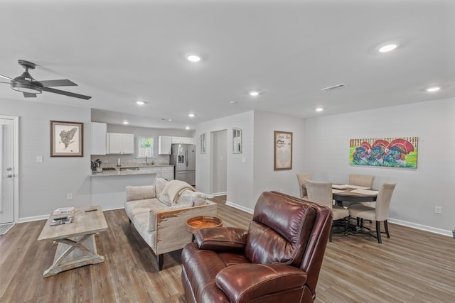 living room featuring light wood-type flooring, ceiling fan, and sink