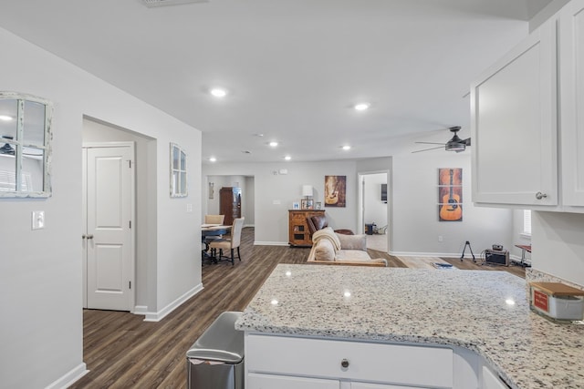 kitchen with light stone countertops, dark wood finished floors, a peninsula, ceiling fan, and white cabinetry