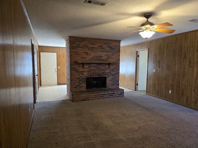 unfurnished living room with a textured ceiling, ceiling fan, wood walls, and a brick fireplace