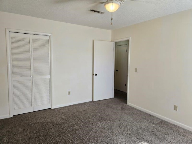 unfurnished bedroom with a textured ceiling, ceiling fan, a closet, and dark colored carpet