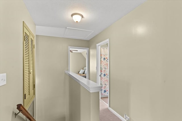 corridor featuring carpet floors, attic access, baseboards, and a textured ceiling