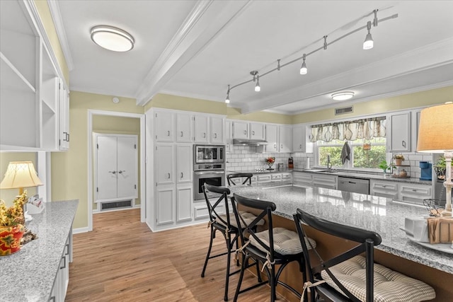 kitchen with light stone counters, a breakfast bar area, visible vents, appliances with stainless steel finishes, and light wood-type flooring