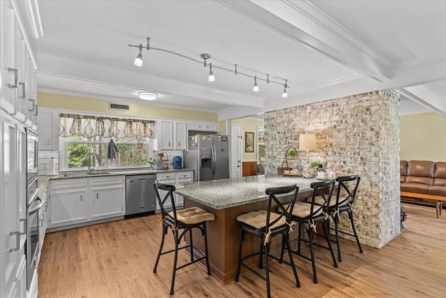 kitchen with visible vents, light wood-style flooring, a breakfast bar, light stone countertops, and stainless steel appliances