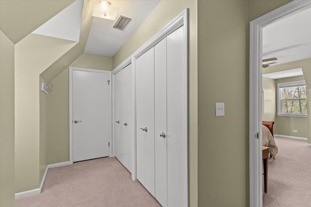 hallway with baseboards, visible vents, and light colored carpet