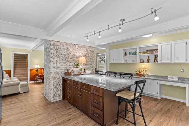 kitchen featuring light stone counters, a breakfast bar, beam ceiling, light wood-style flooring, and white cabinetry