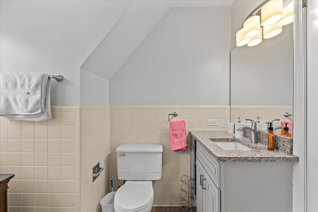 half bathroom with toilet, a wainscoted wall, lofted ceiling, vanity, and tile walls