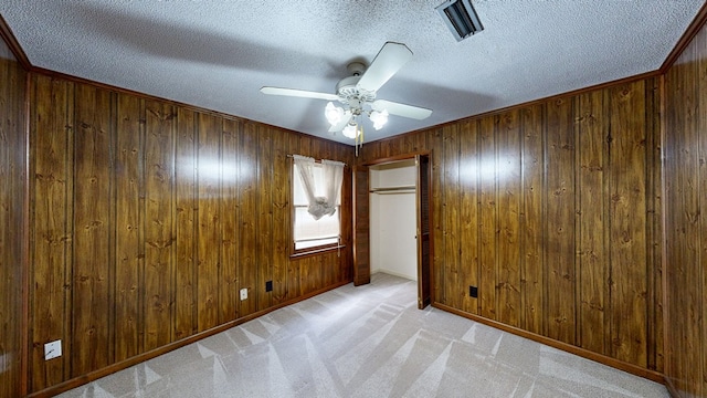 unfurnished room featuring a ceiling fan, a textured ceiling, wood walls, and light carpet