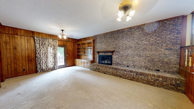 unfurnished living room with a brick fireplace, a ceiling fan, wood walls, and light carpet