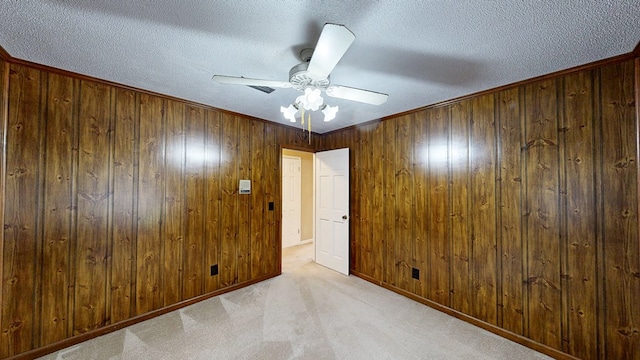 spare room with carpet floors, wood walls, baseboards, a textured ceiling, and a ceiling fan