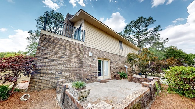 view of side of home featuring a patio, a balcony, and brick siding