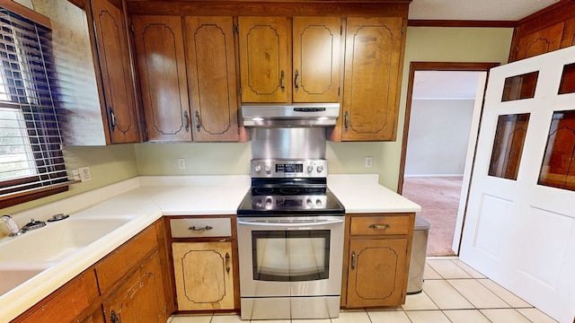 kitchen with electric range, a sink, light countertops, brown cabinetry, and under cabinet range hood