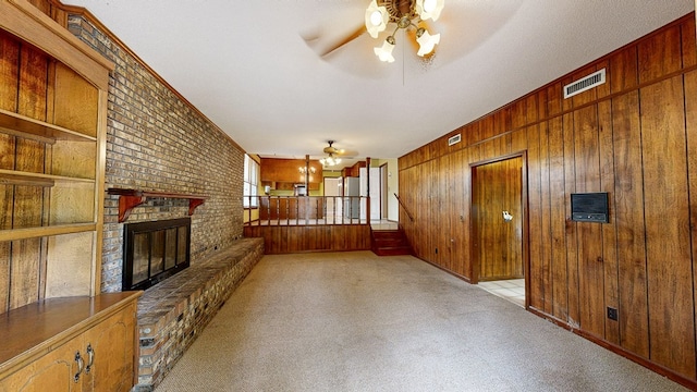 unfurnished living room featuring visible vents, wood walls, a fireplace, ceiling fan, and carpet flooring