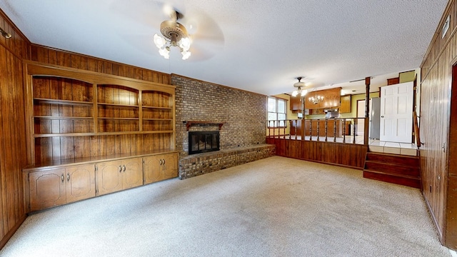 unfurnished living room featuring a fireplace, a ceiling fan, wood walls, and light carpet