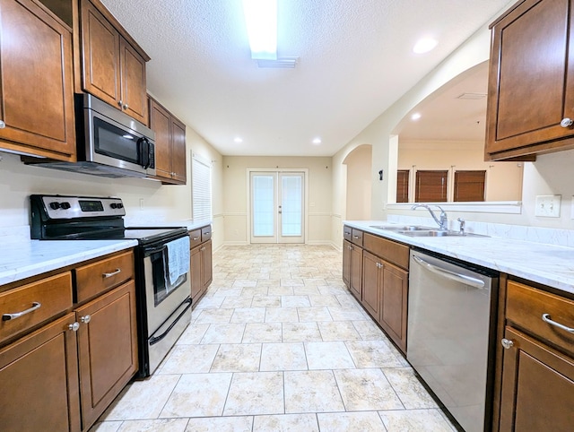 kitchen featuring arched walkways, appliances with stainless steel finishes, light stone countertops, a textured ceiling, and a sink