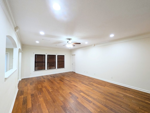 empty room featuring arched walkways, baseboards, hardwood / wood-style flooring, and crown molding