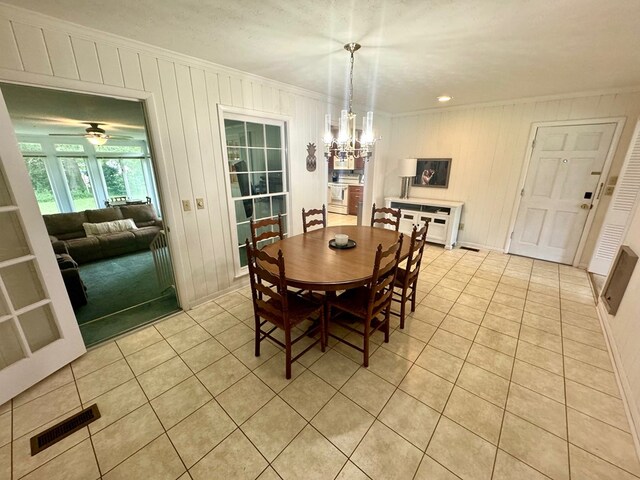 tiled dining area with ceiling fan with notable chandelier, wooden walls, and crown molding