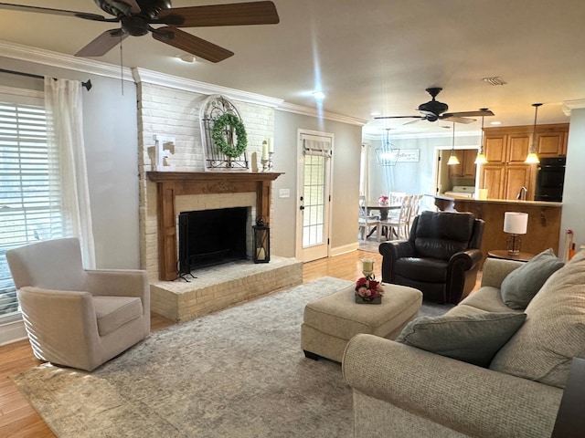 living room featuring crown molding, ceiling fan, a fireplace, and light wood-type flooring