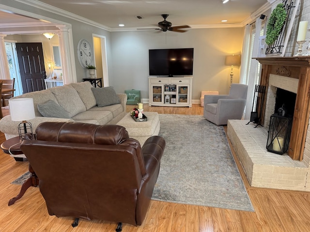 living room with a brick fireplace, crown molding, light hardwood / wood-style flooring, and ornate columns