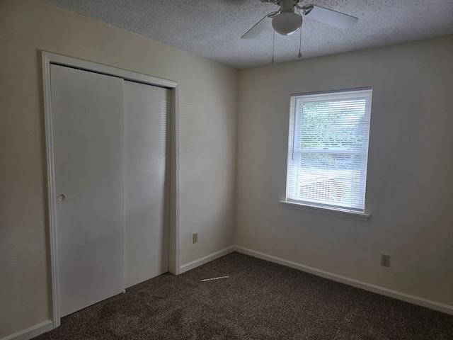 unfurnished bedroom featuring a closet, dark colored carpet, baseboards, ceiling fan, and a textured ceiling