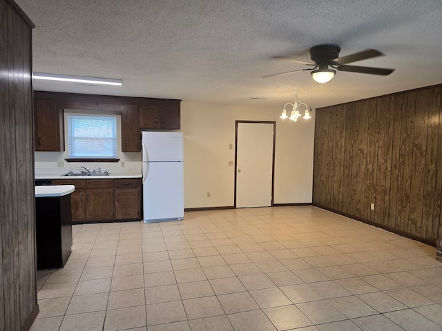 kitchen with freestanding refrigerator, wood walls, a sink, and light countertops